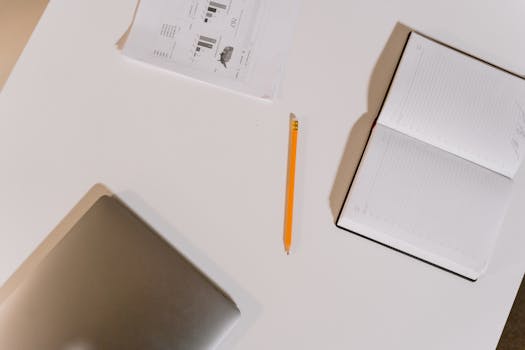 Top view of a modern office desk with a laptop, notebook, and pencil showcasing productivity.